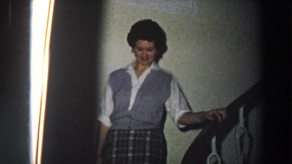 Woman in 1950s-style clothing descends an interior staircase in Italy, her hand on the wooden railing.