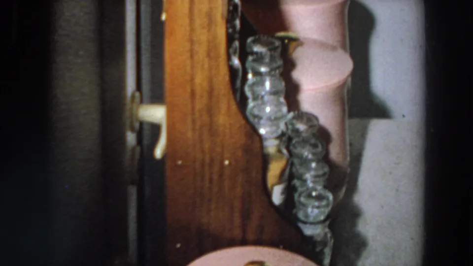 The camera pans along the wooden shelf, showing glass jars and a pink household container in a 1958 Italian interior.