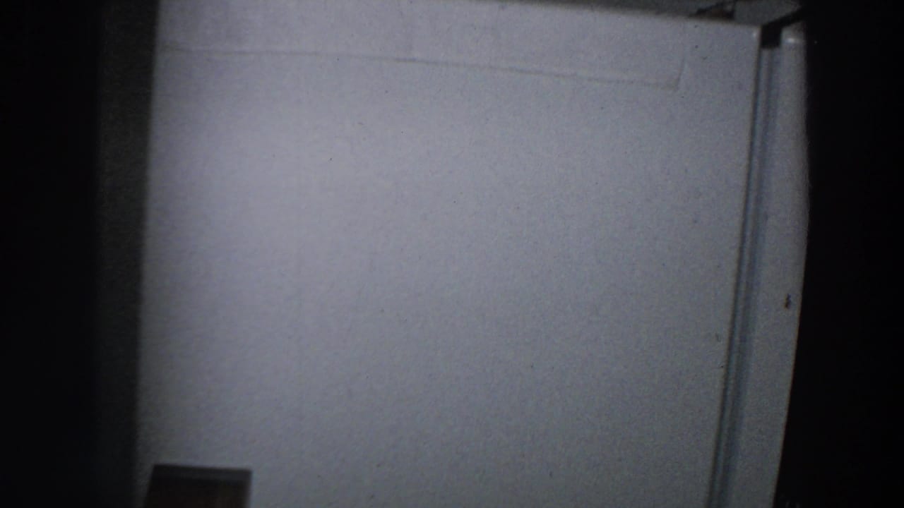 Dim kitchen view with a white refrigerator door and dark vertical film edge.