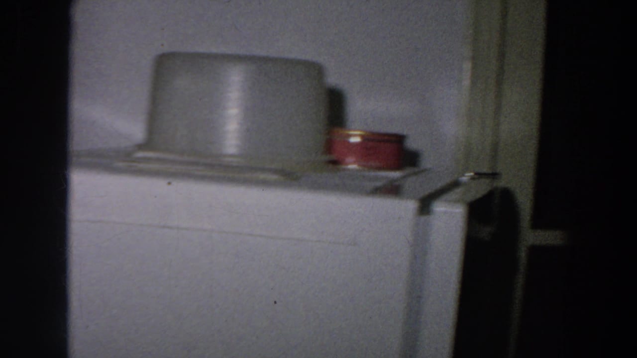 1958 8mm frame from Italy showing the top of a refrigerator with a pale container and small red can in a modest kitchen.