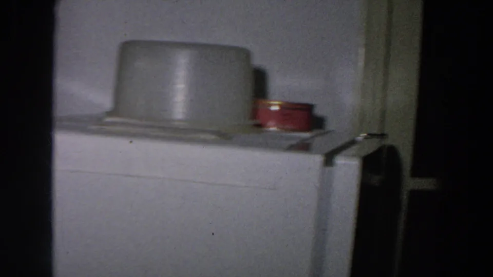 1958 8mm frame from Italy showing the top of a refrigerator with a pale container and small red can in a modest kitchen.