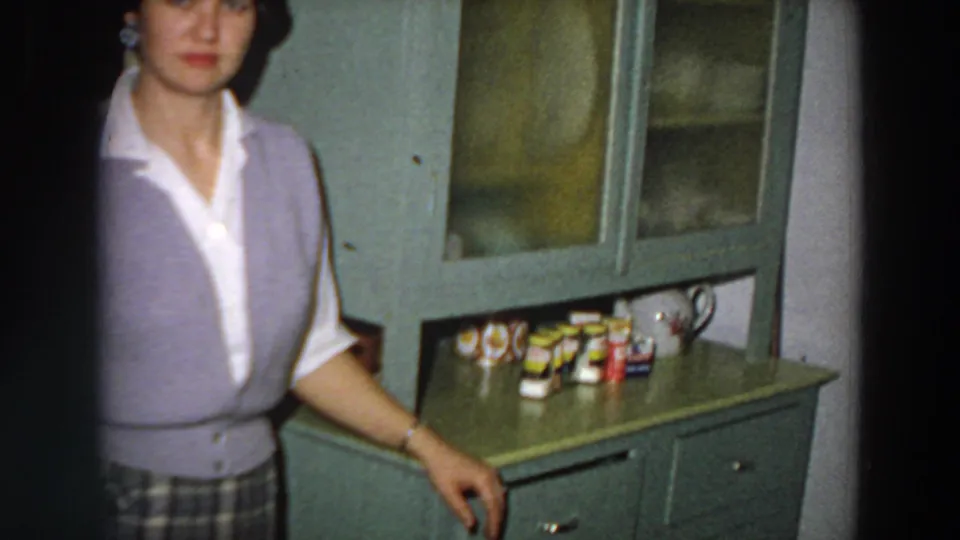 A cropped home-movie view shows the woman beside a green cabinet topped with small tins and containers in the Italy kitchen setting.