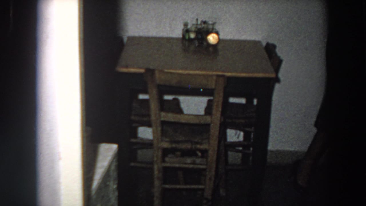1958 Italian kitchen or dining corner with a brown wooden table, chairs, and a small lamp visible in soft 8mm exposure.