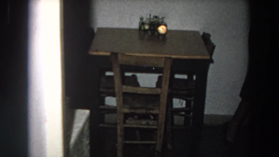 1958 Italian kitchen or dining corner with a brown wooden table, chairs, and a small lamp visible in soft 8mm exposure.