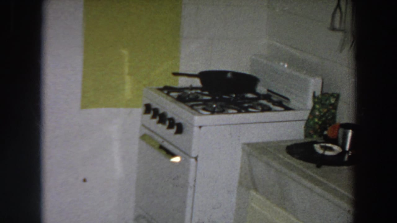 1958 Italian home interior showing a white gas stove, black pan, green wall panel, and nearby counter with a mug and plate.