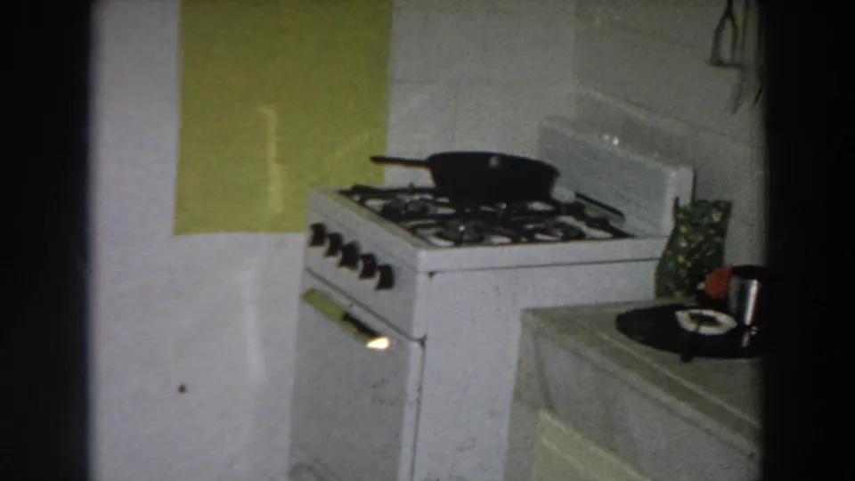 1958 Italian home interior showing a white gas stove, black pan, green wall panel, and nearby counter with a mug and plate.