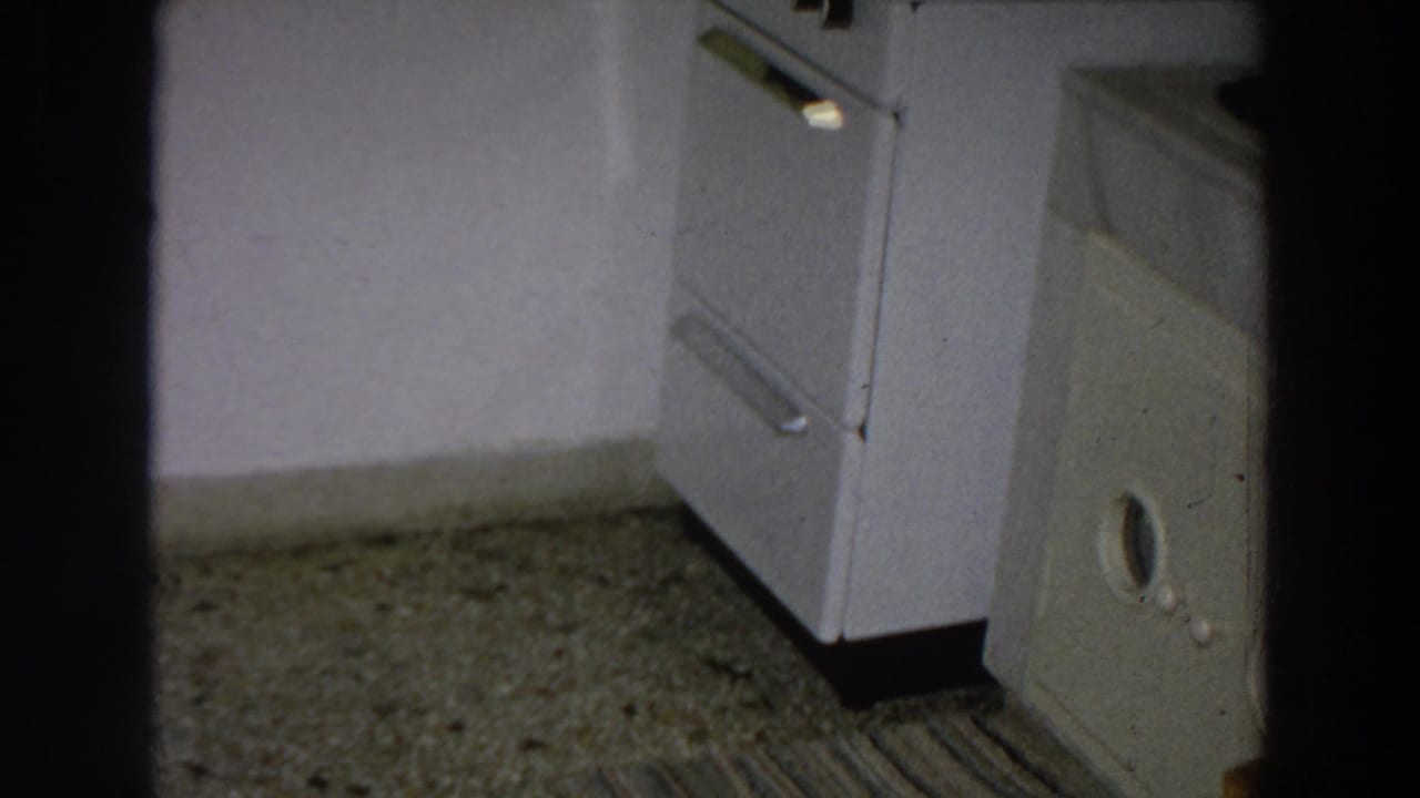 White stove beside a speckled floor and striped rug in a dim kitchen interior.