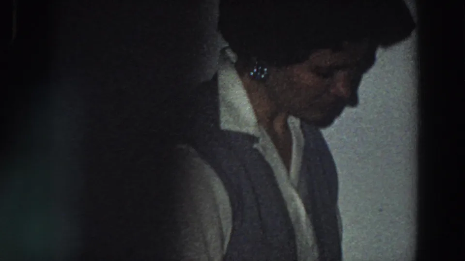 A woman in a white collared shirt and dark vest looks down in a dim private interior, consistent with the Italy 1958 metadata.