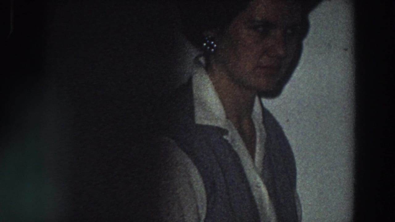 The woman is seen closer in shadow, wearing a white collared shirt and dark vest inside the private Italian home-movie setting.