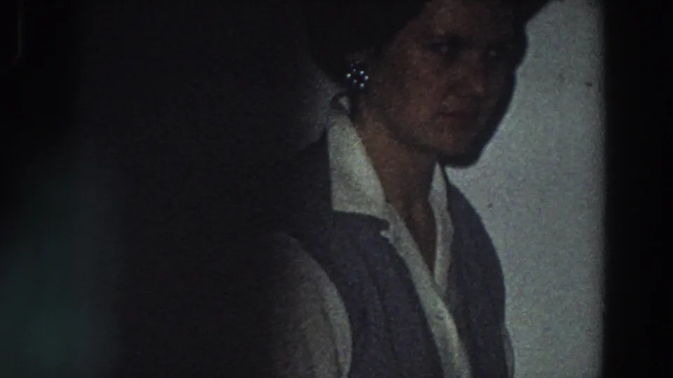The woman is seen closer in shadow, wearing a white collared shirt and dark vest inside the private Italian home-movie setting.
