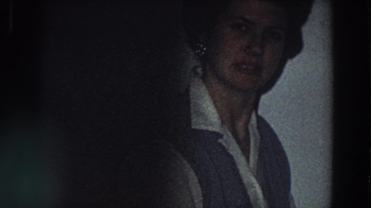 The woman remains near the tiled kitchen wall, her face partly shadowed in grainy 1958 Italy home-movie footage.