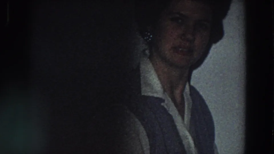 The woman remains near the tiled kitchen wall, her face partly shadowed in grainy 1958 Italy home-movie footage.