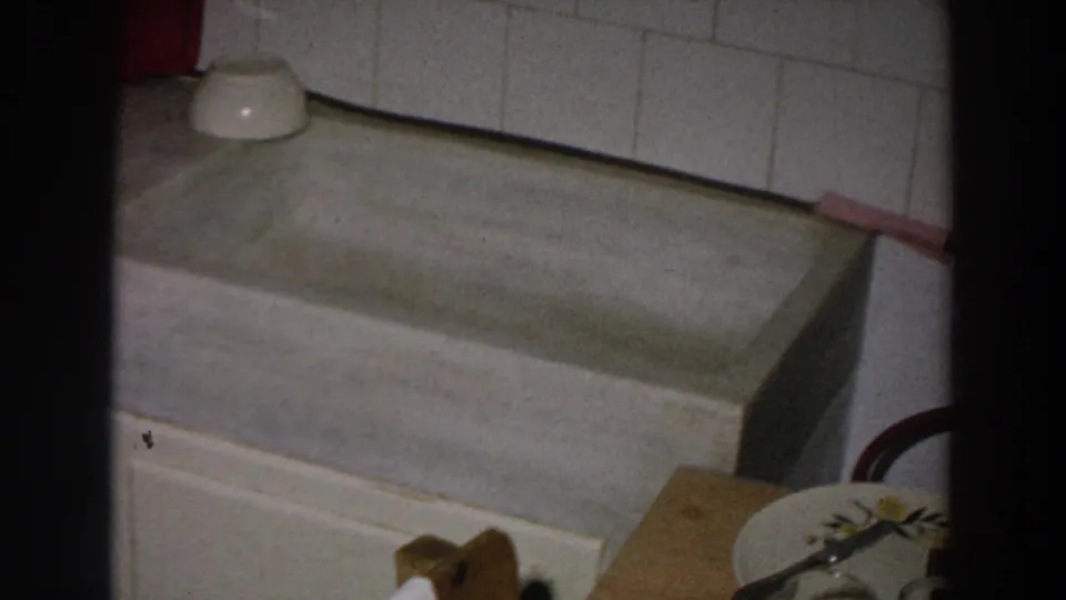 The camera settles on the deep sink basin and tiled wall, with a small bowl, cloth, and partial dish visible at frame edge.