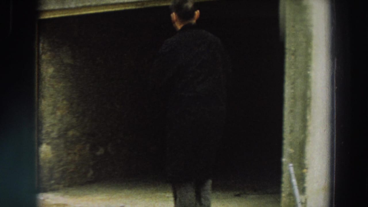 The man approaches or looks into a dark entrance beside a shuttered industrial-looking exterior in Italy.