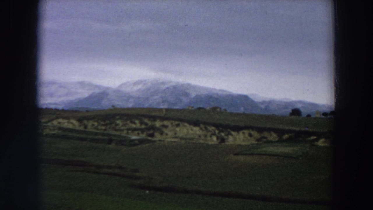Green countryside and distant snowy mountains seen through dark film-frame borders.