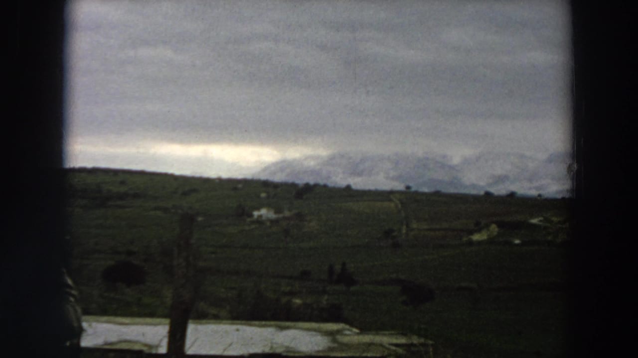 Rural fields and distant mountains under a cloudy sky, seen through dark film gate edges.