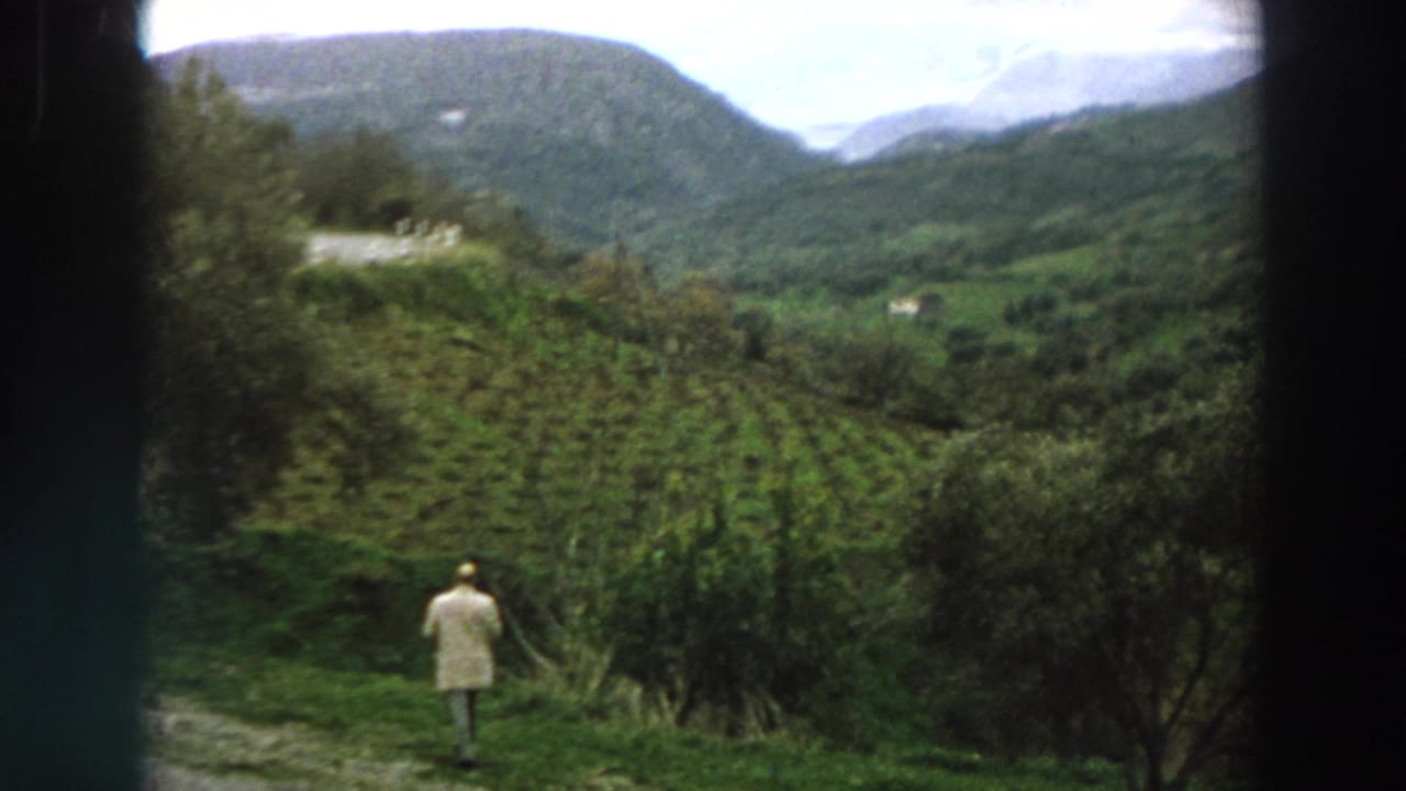 1958 Italy home-movie frame with a man walking into a hillside field overlooking a green mountain valley.
