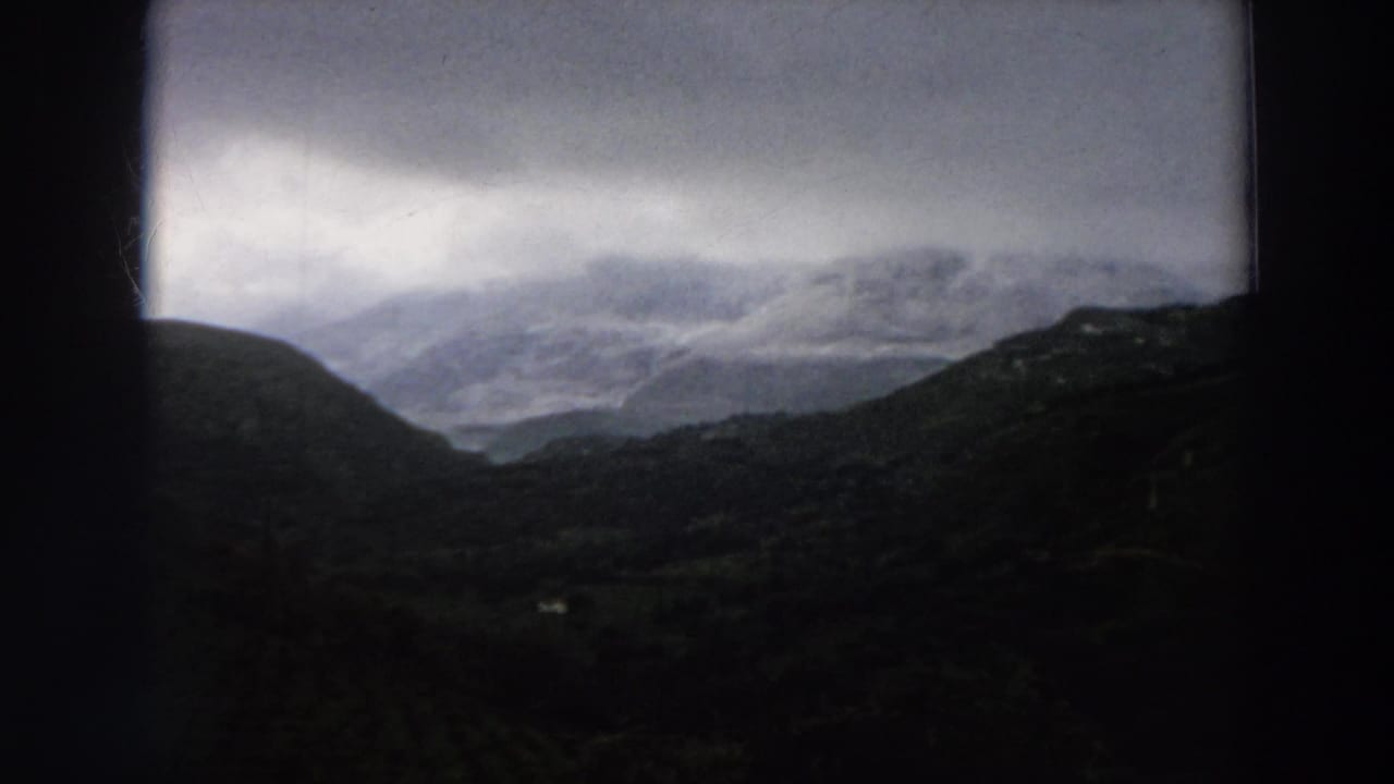 A 1958 Italy travel frame shows layered hills and a misty mountain range beneath a cloudy sky.