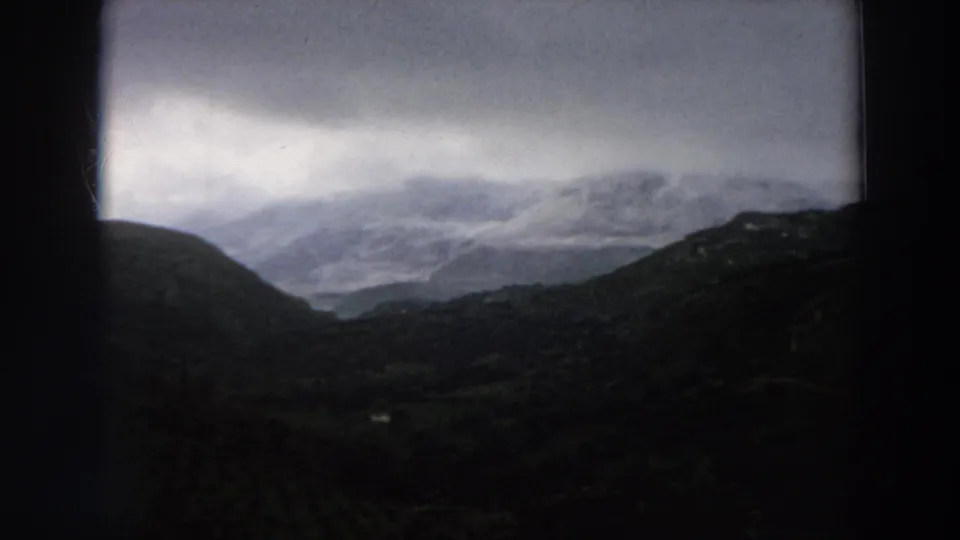 A 1958 Italy travel frame shows layered hills and a misty mountain range beneath a cloudy sky.
