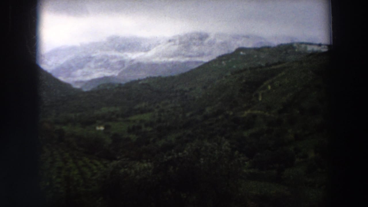 Vintage 8mm view of Italian mountain country in 1958, with green slopes leading toward a misty peak.