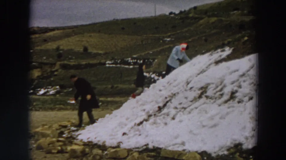 1958 Italy 8mm frame showing people near a large snow pile on a rural hillside under an overcast sky.