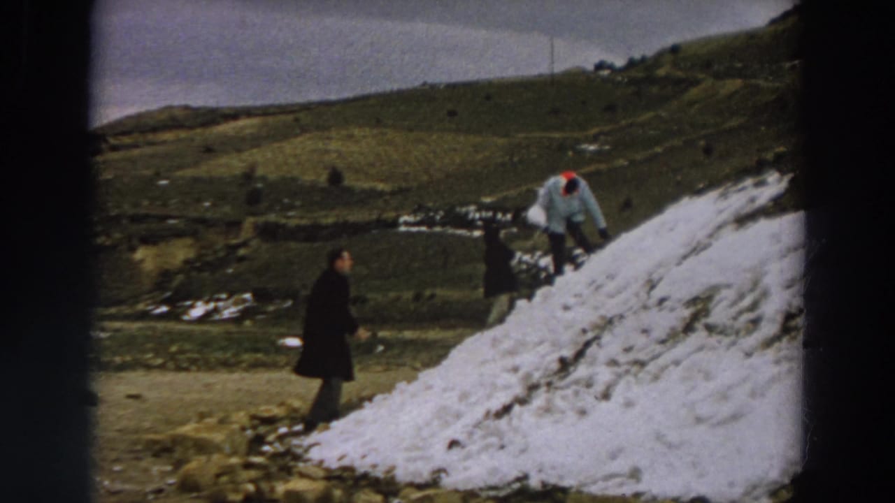 1958 Italy home-movie frame with one person in a dark coat and another in a light jacket on a snowy mound.