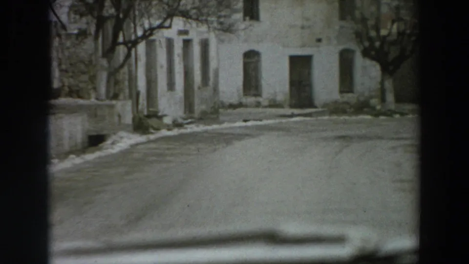 1958 Italy street view with pale stucco facades, dark doorways, bare trees, a curving road, and snow along the edges.