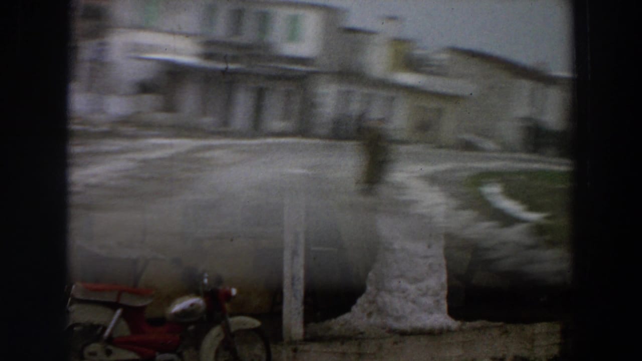 Blurred view of a snowman near a yellow building with a red scooter at lower left.