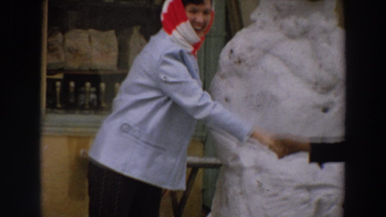 A woman in a light jacket and red headscarf shakes hands beside a large white sculpture in the Italy 1958 home-movie scene.