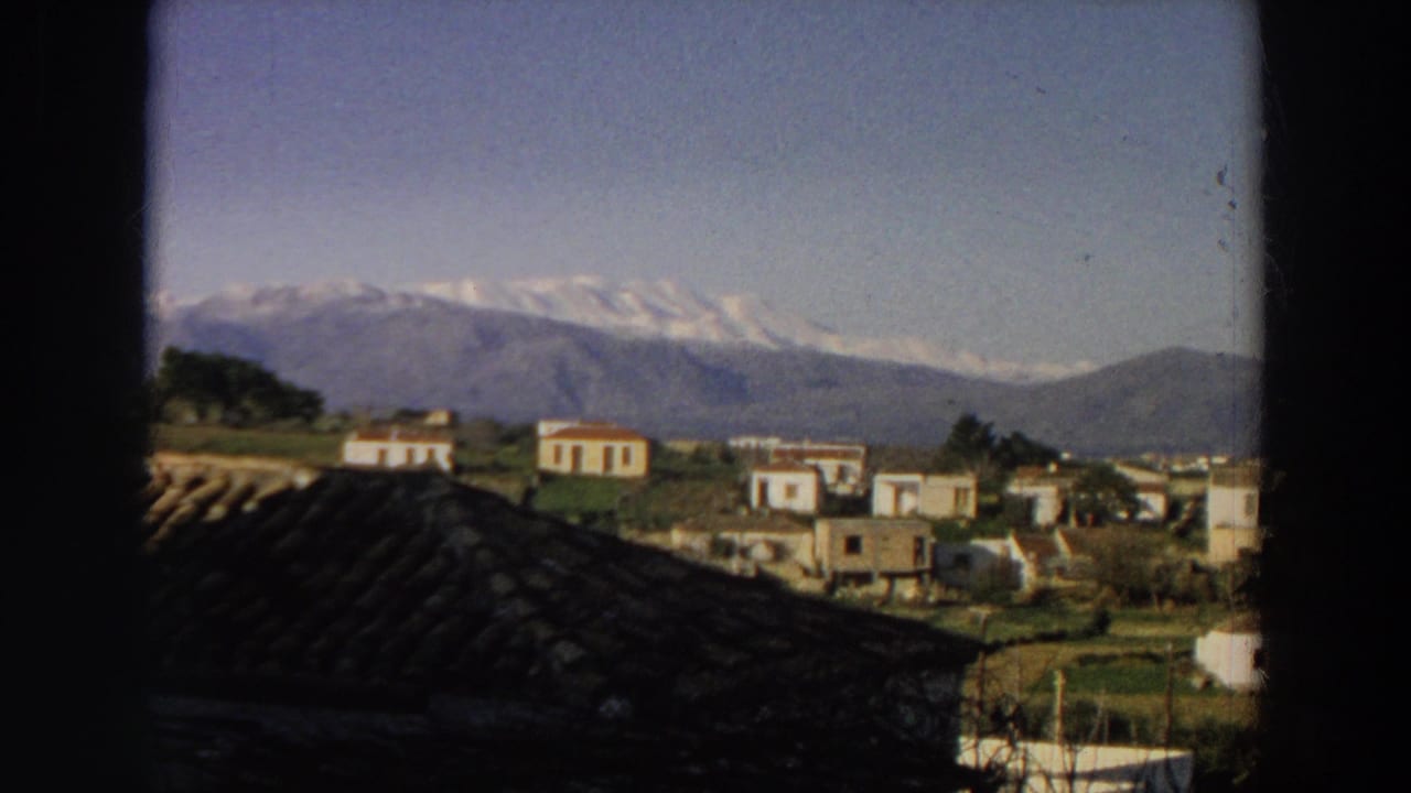 1958 Italy landscape view with white hillside buildings, green fields, a tiled foreground roof, and distant mountain peaks.