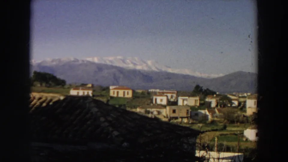 1958 Italy landscape view with white hillside buildings, green fields, a tiled foreground roof, and distant mountain peaks.