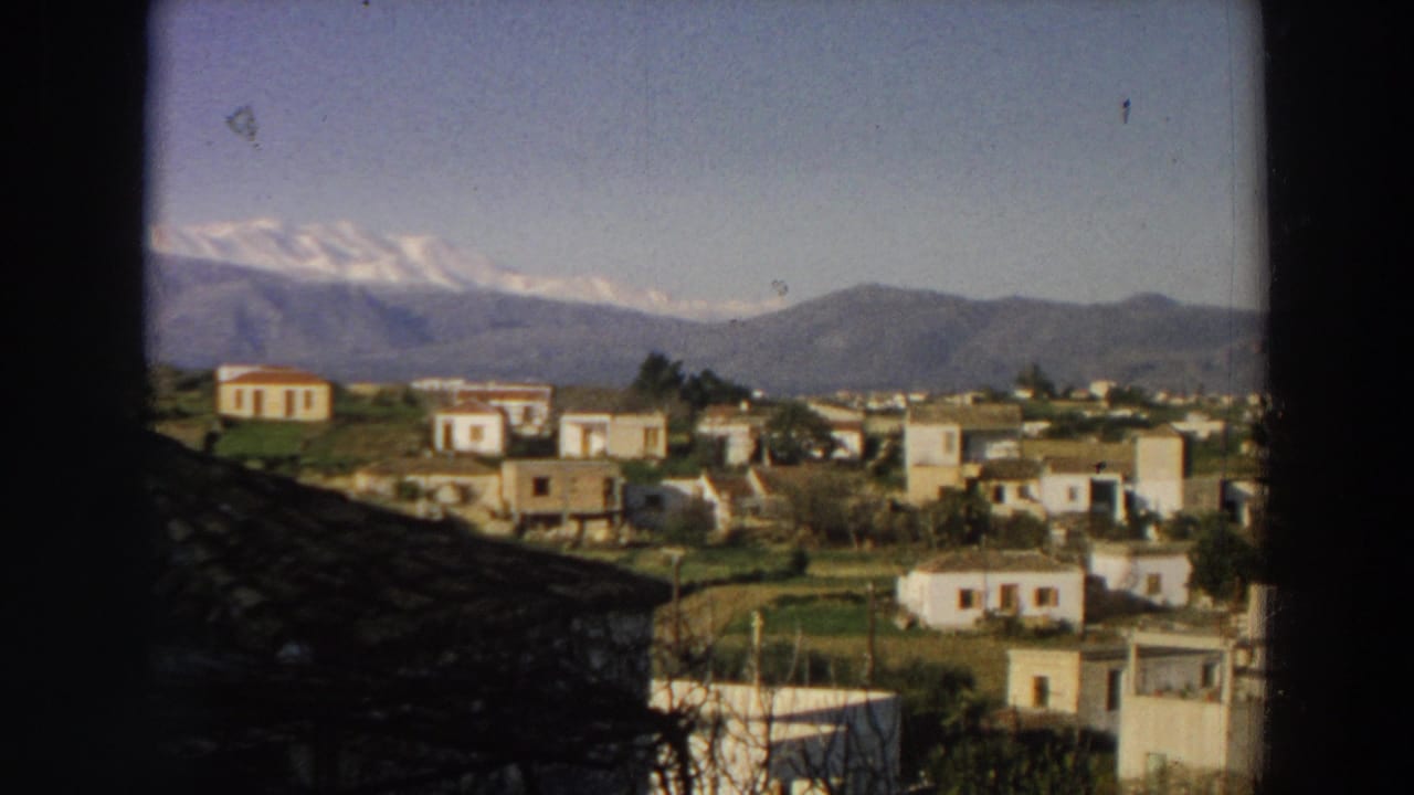 1958 Italy home-movie frame with pale hillside houses, fields, bare branches, and layered mountains in the background.