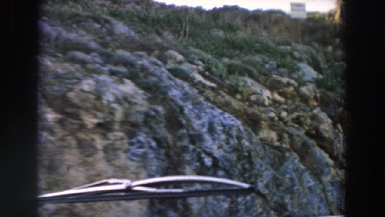 1958 Italy vehicle-window frame showing a rocky hillside, sparse vegetation, and a windshield wiper across the lower foreground.