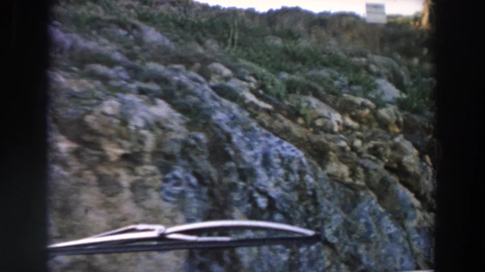 1958 Italy vehicle-window frame showing a rocky hillside, sparse vegetation, and a windshield wiper across the lower foreground.