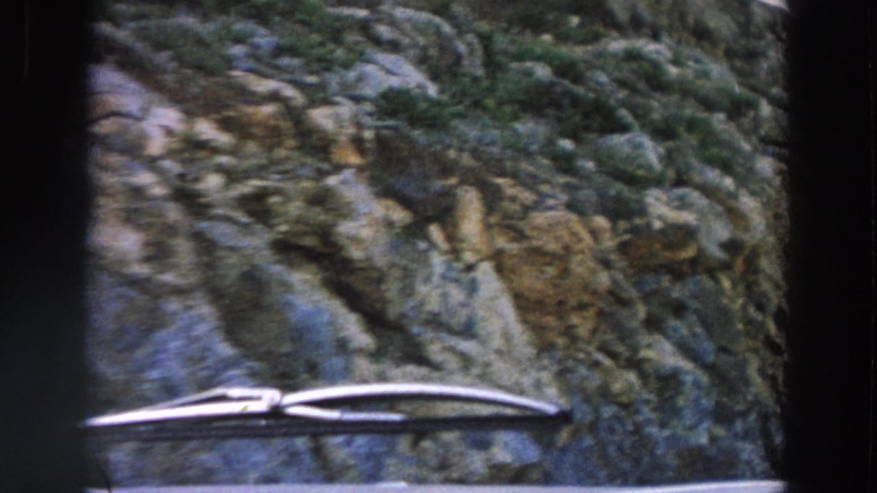Car windshield view passing a rocky roadside with wipers visible at the bottom.