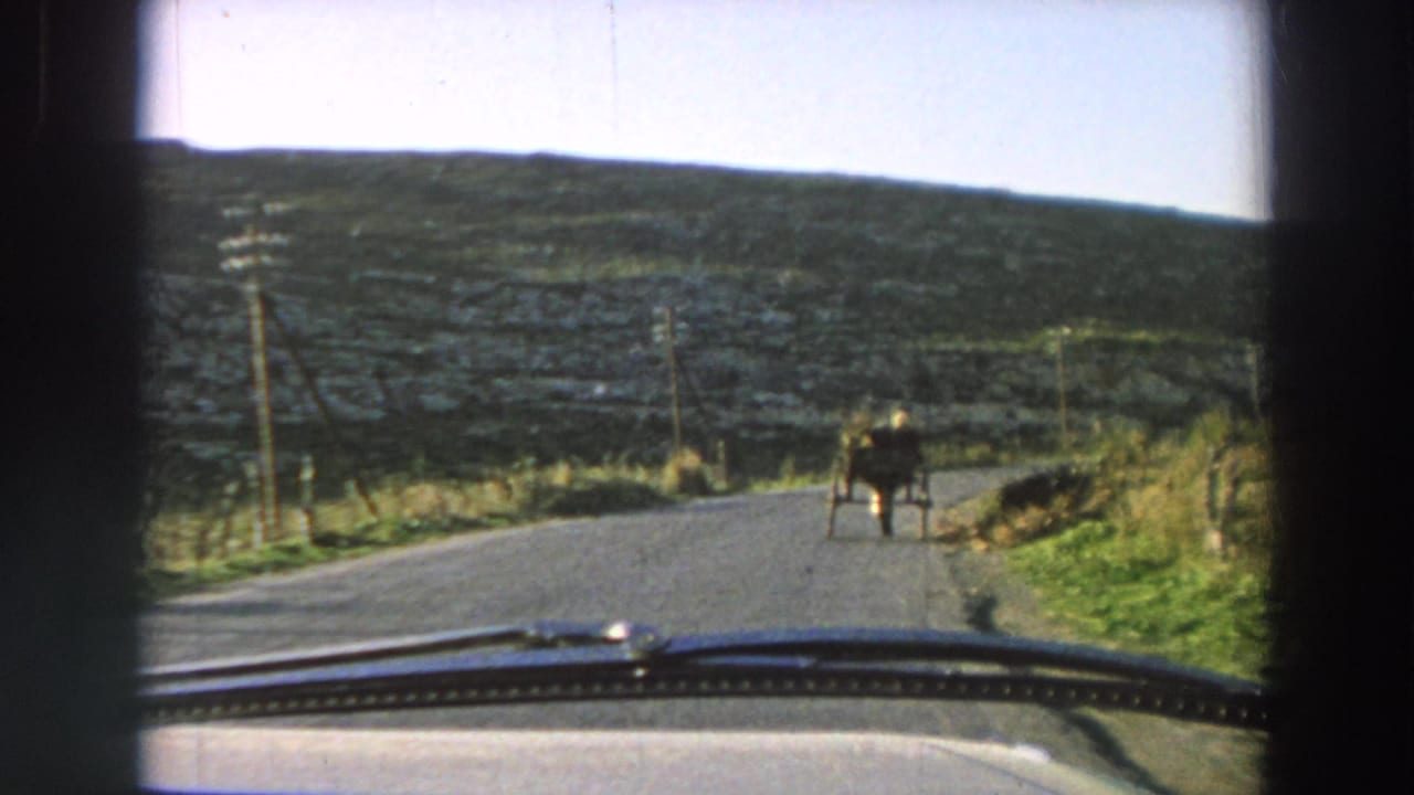 Car windshield view of a rural road with a horse-drawn cart ahead.