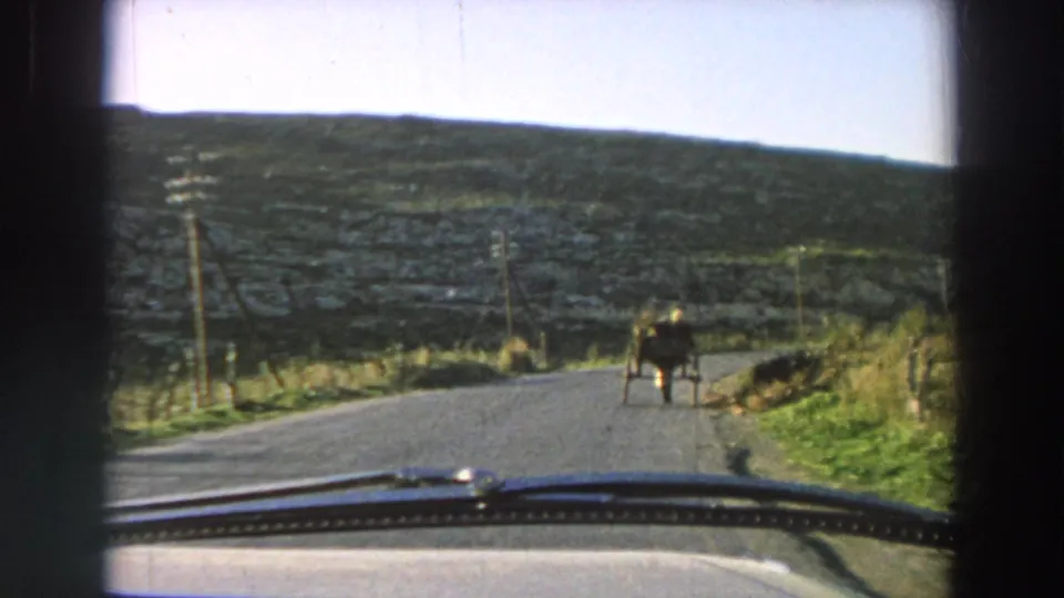 1958 Italy 8mm frame from inside a car, looking down a rural road toward a horse-drawn cart in hilly countryside.