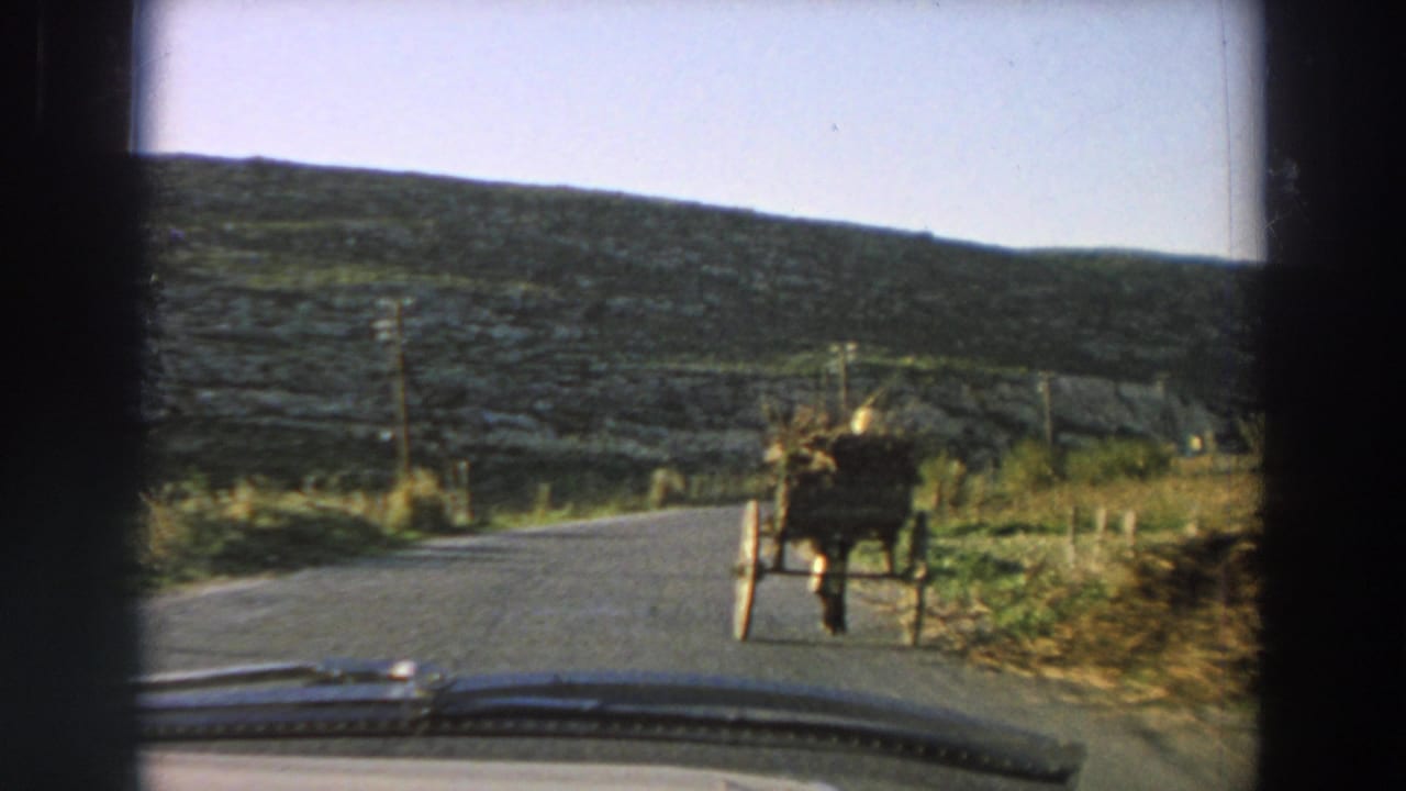 1958 Italy home-movie frame showing a horse-drawn cart on a narrow road seen through a car windshield.