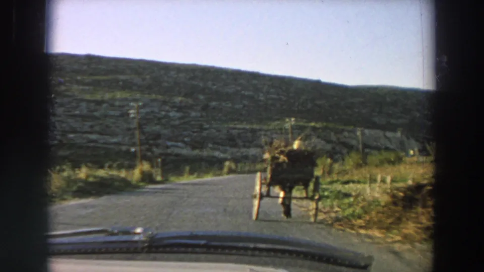 1958 Italy home-movie frame showing a horse-drawn cart on a narrow road seen through a car windshield.