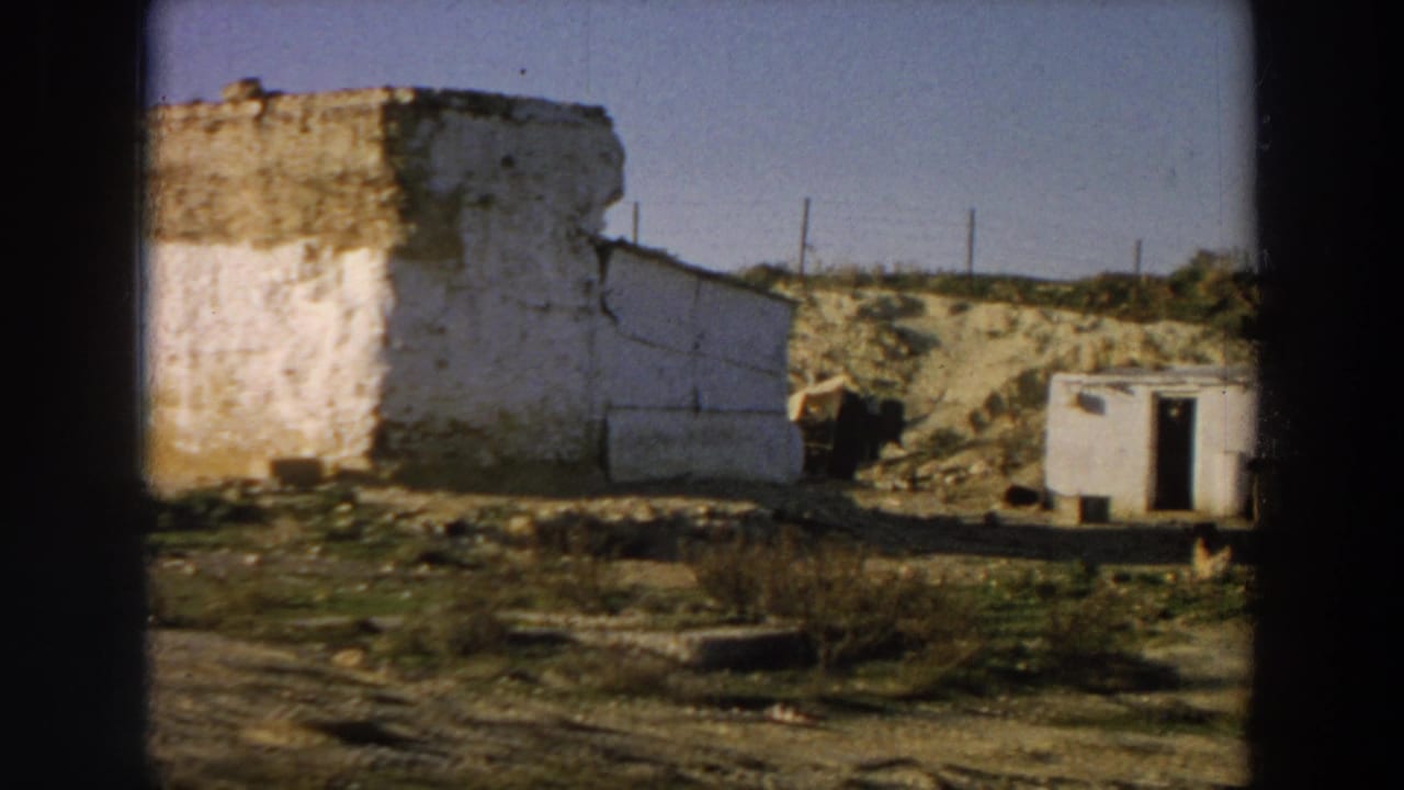 Whitewashed crumbling building beside dry ground and a small outbuilding.