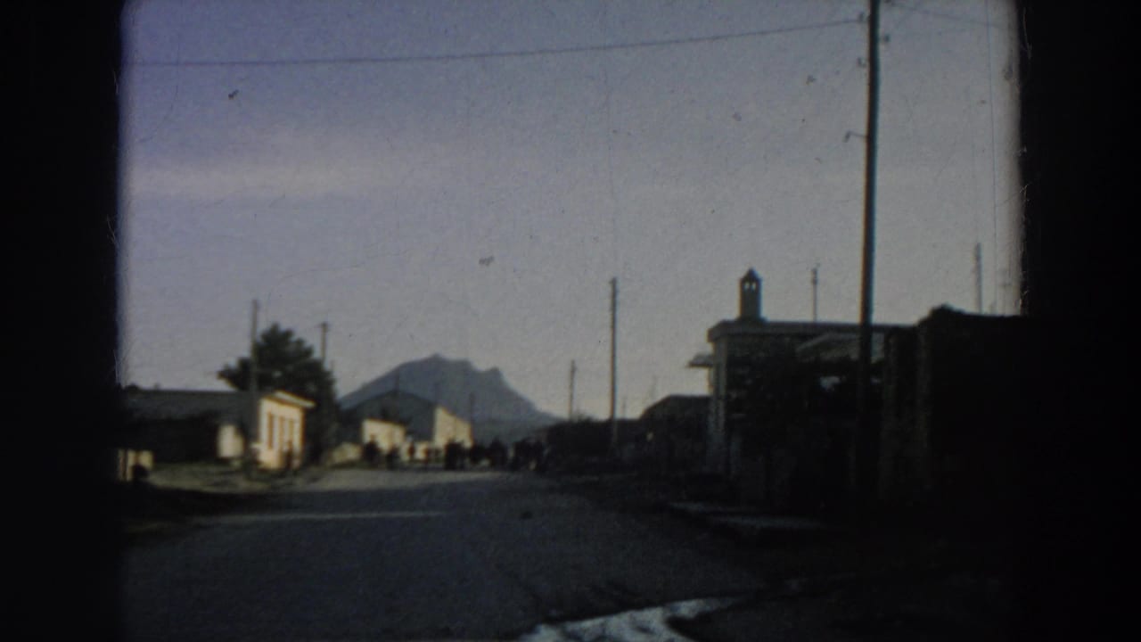 Road leading toward small buildings with a distant mountain and people ahead.