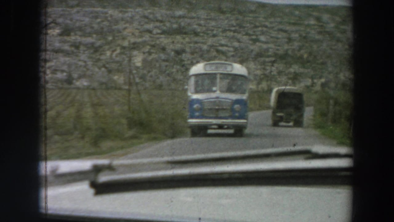 Blue-and-white bus approaches on a narrow road seen through a car windshield.