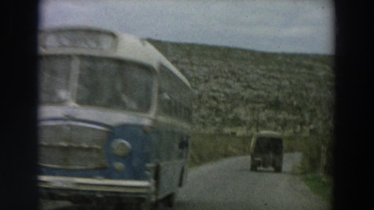 Bus passes close to the camera while a covered truck continues ahead on the road.