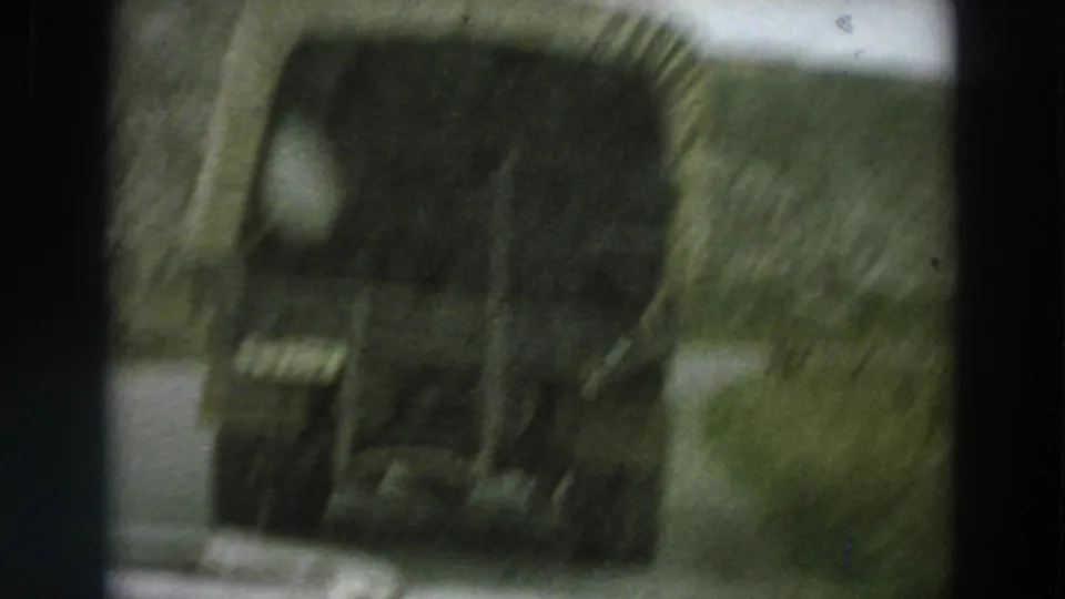 A close, blurred rear view of a canvas-covered truck fills the frame during a moving-car shot on an Italian country road.