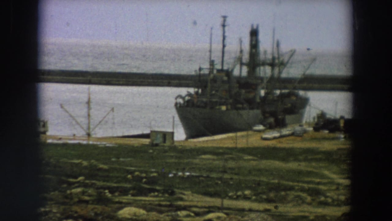1958 Italy 8mm frame with the moored ship filling the right side, pier details, water, and shoreline infrastructure nearby.