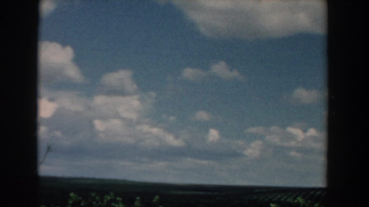 1958 South Carolina home-movie frame showing scattered clouds over a low, flat rural field horizon from a moving vehicle.
