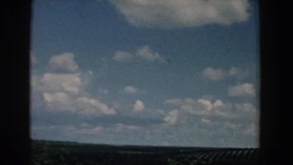1958 South Carolina 8mm view of open blue sky, cumulus clouds, and a distant flat field line seen in motion.