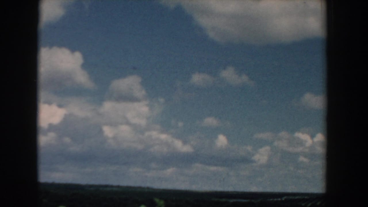 Cloud-filled blue sky over a distant dark landscape, divided by black frame edges.