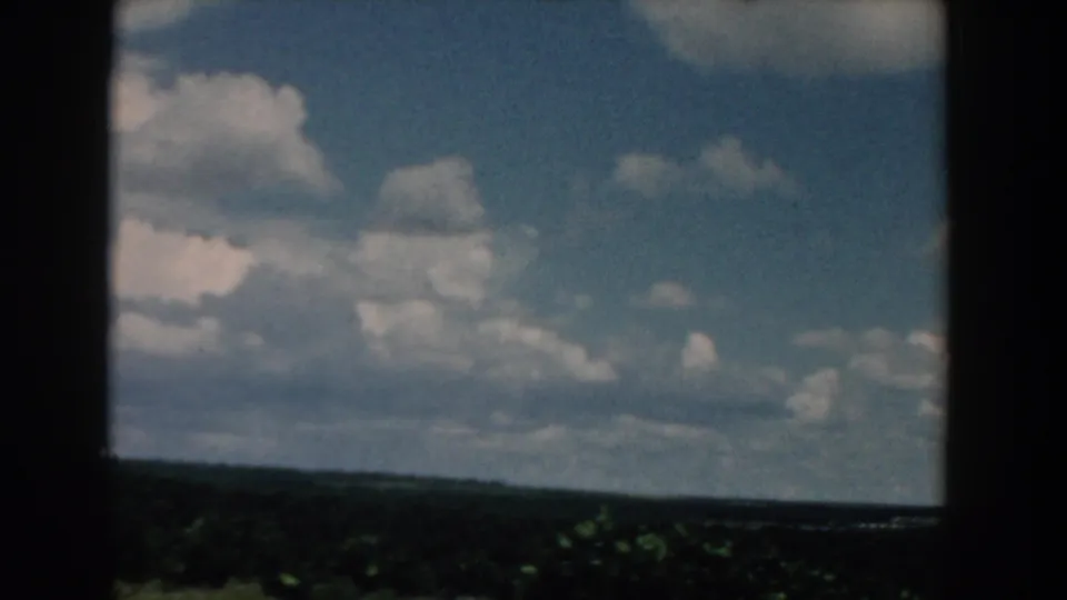 1958 South Carolina 8mm frame of scattered clouds and distant landscape, with dark window-like divisions in the foreground.