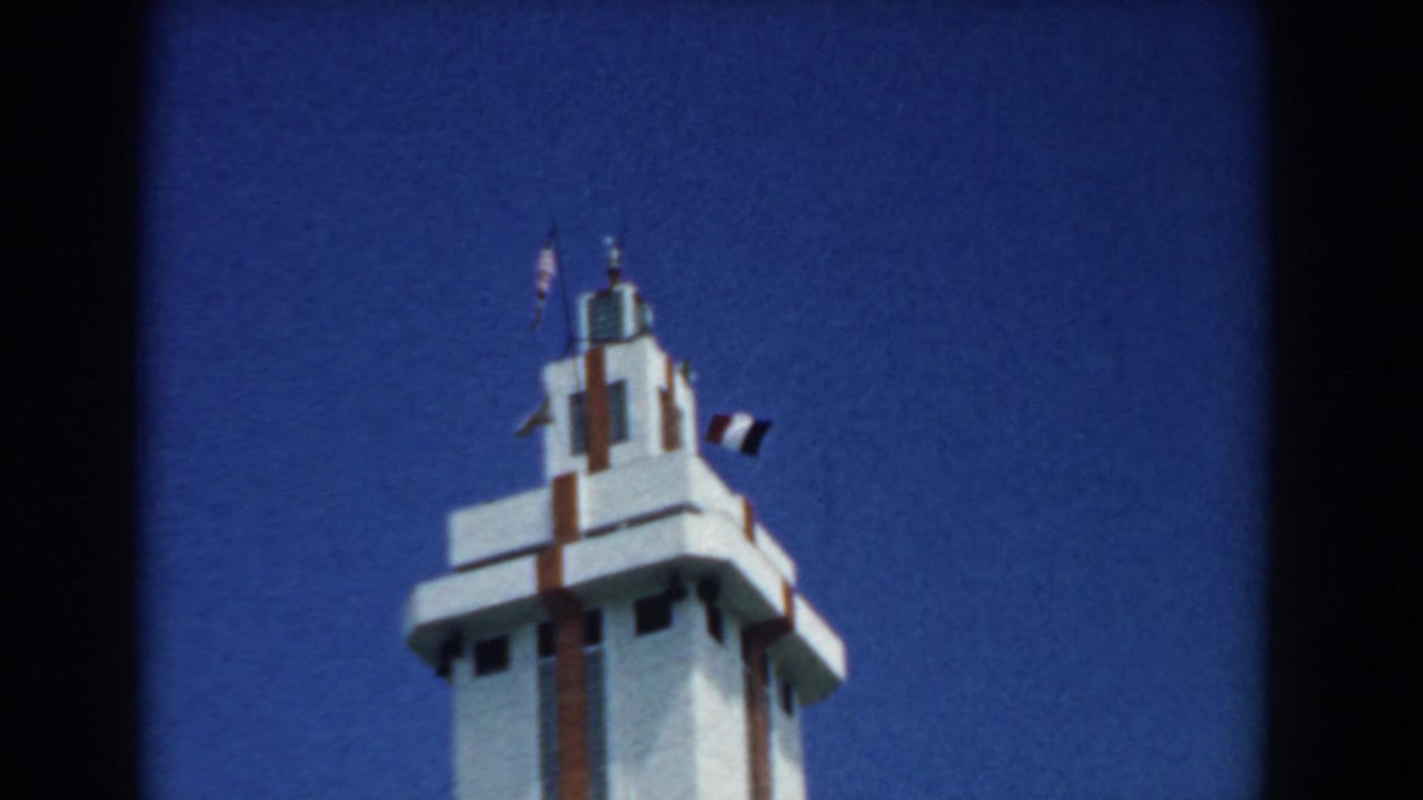 Top of a white tower with flags against a blue sky.